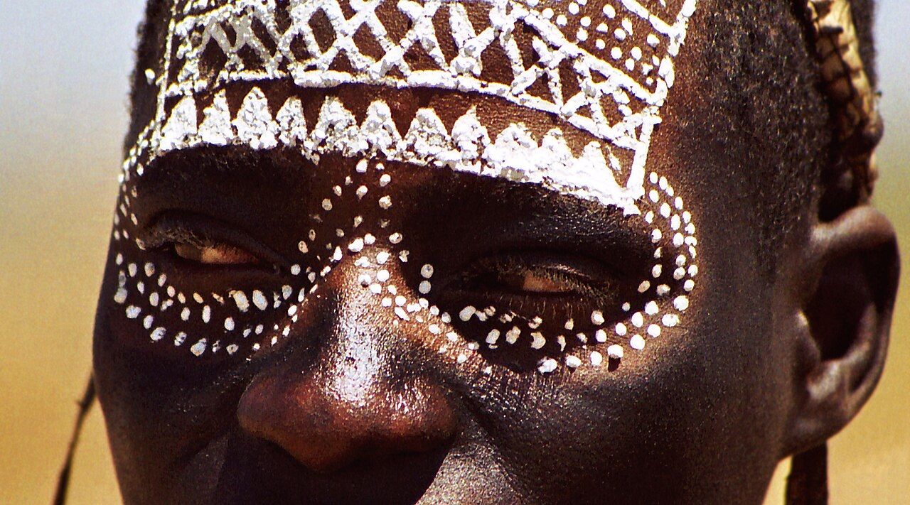 A young Maasai initiate whose face has been painted with ritual designs marking his initiation status
