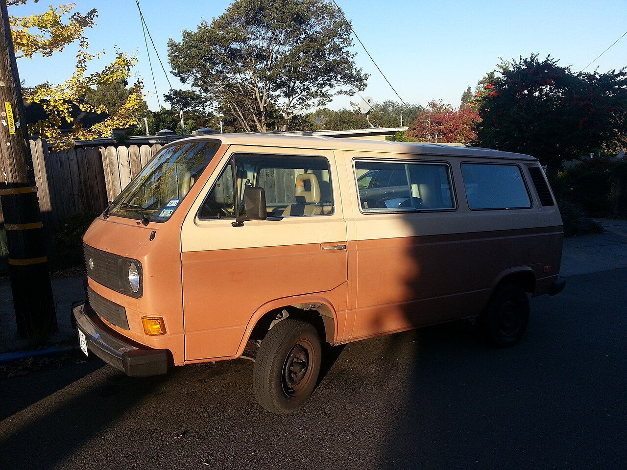 A two-tone 1983 Volkswagen Vanagon diesel van parked at the curb of a residential street in late afternoon sunlight