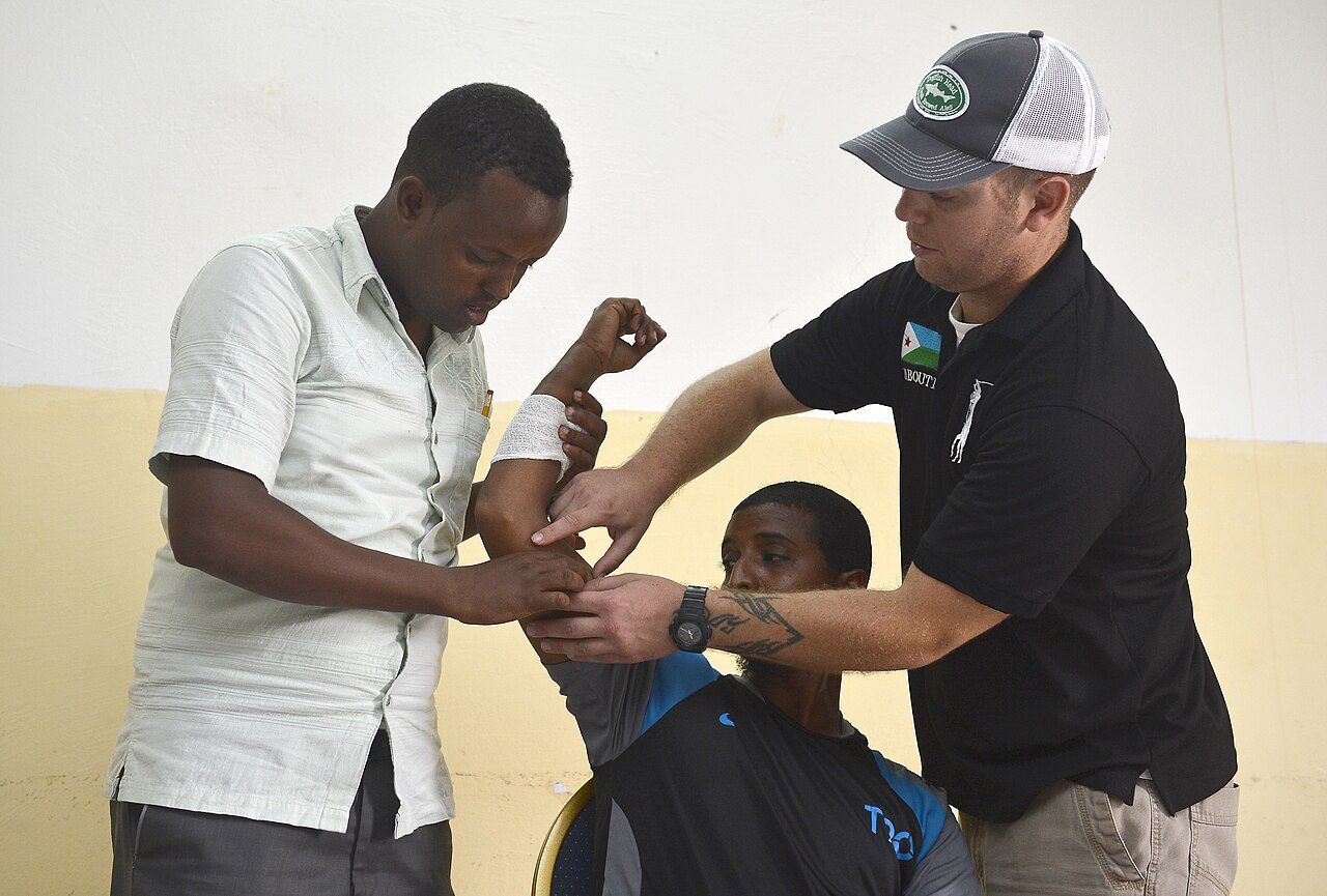 A community health worker measuring a patient&rsquo;s blood pressure at a table in a neighbourhood clinic setting