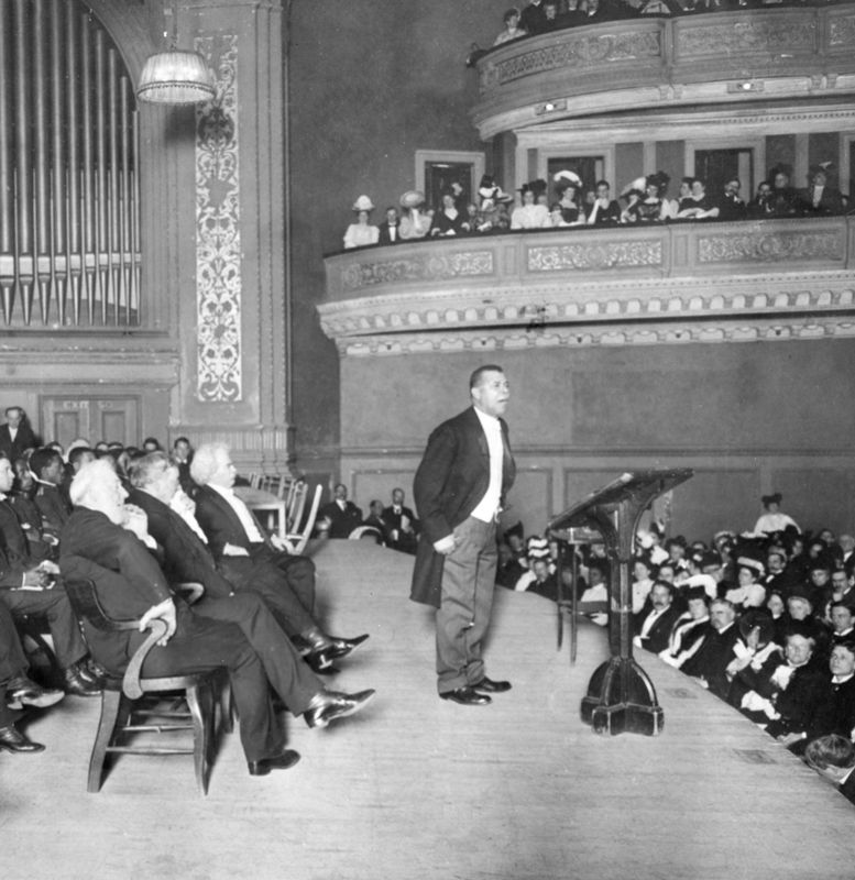 A lecture hall photographed from the stage, showing rows of listeners with varied expressions and postures