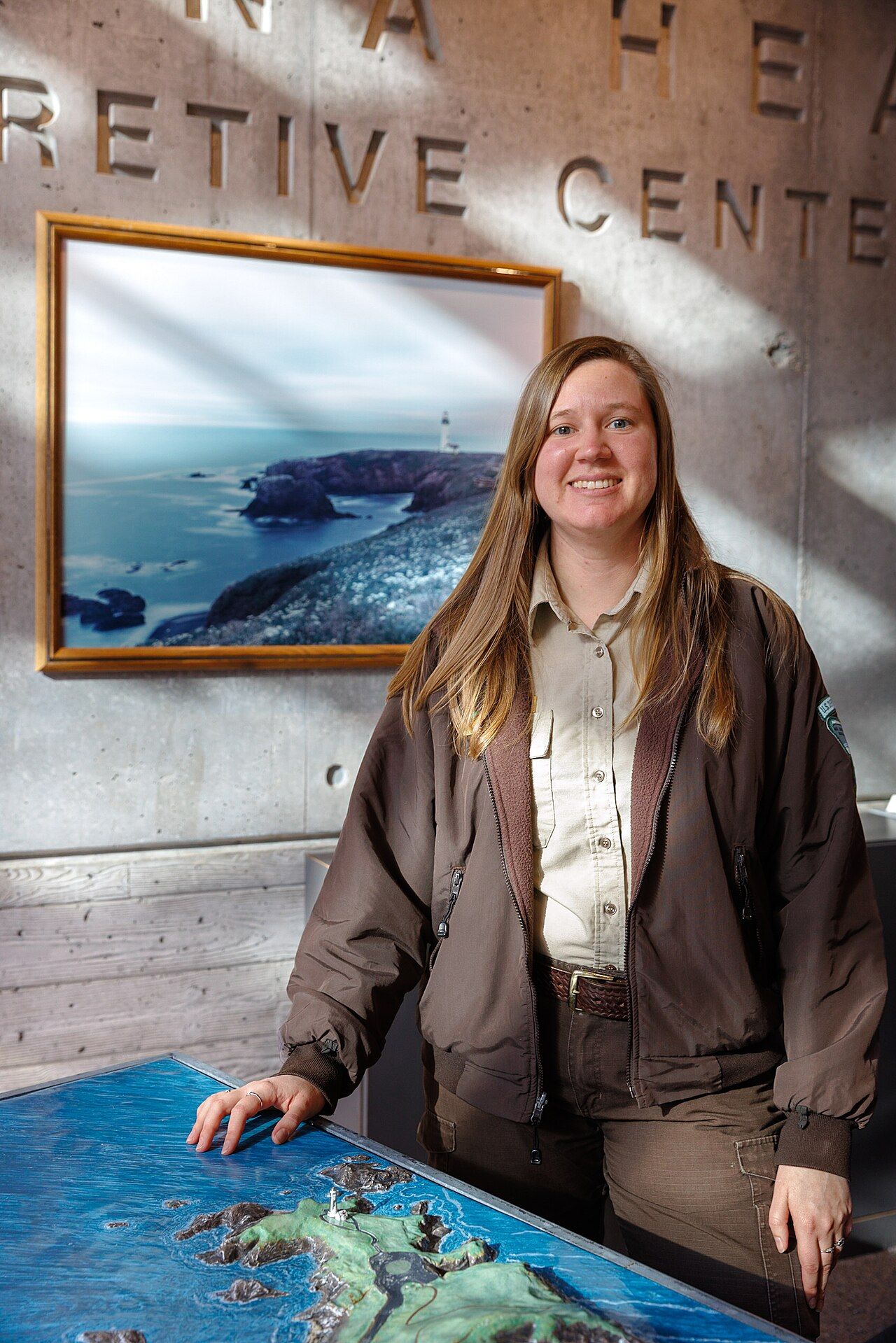 A single staff member standing beside a large relief map at an interpretive centre, facing the camera