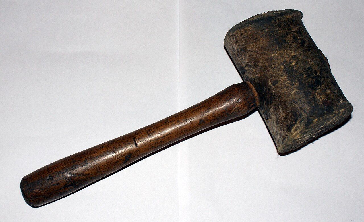 A wooden printer's type case with compartments holding metal letters of different sizes, beside a composing stick with set type.