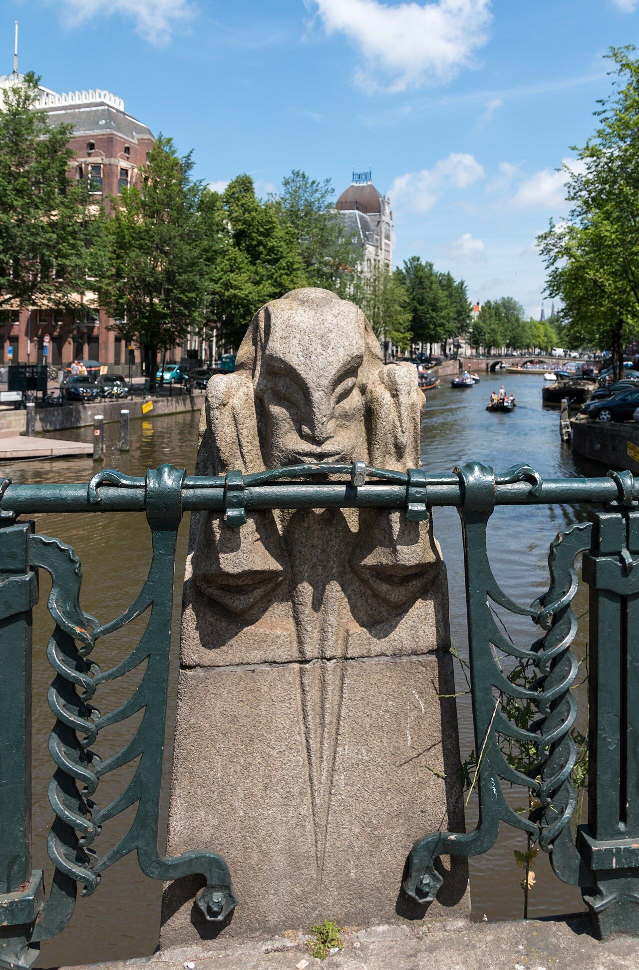 Colour photograph of a stone bridge over the Keizersgracht canal in Amsterdam, with tall canalside buildings, parked cars and small boats
