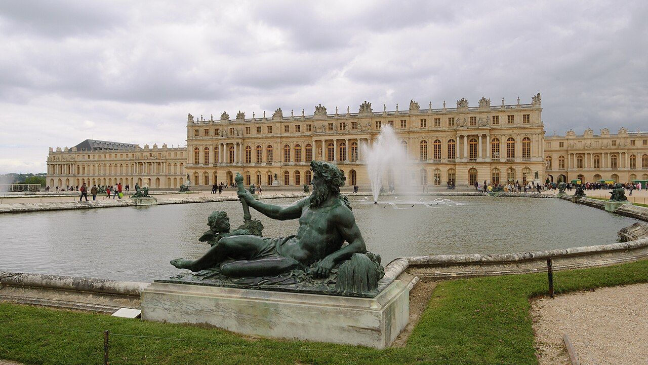 The Palace of Versailles seen from the gardens, with its long classical facade, formal parterres and reflecting basins